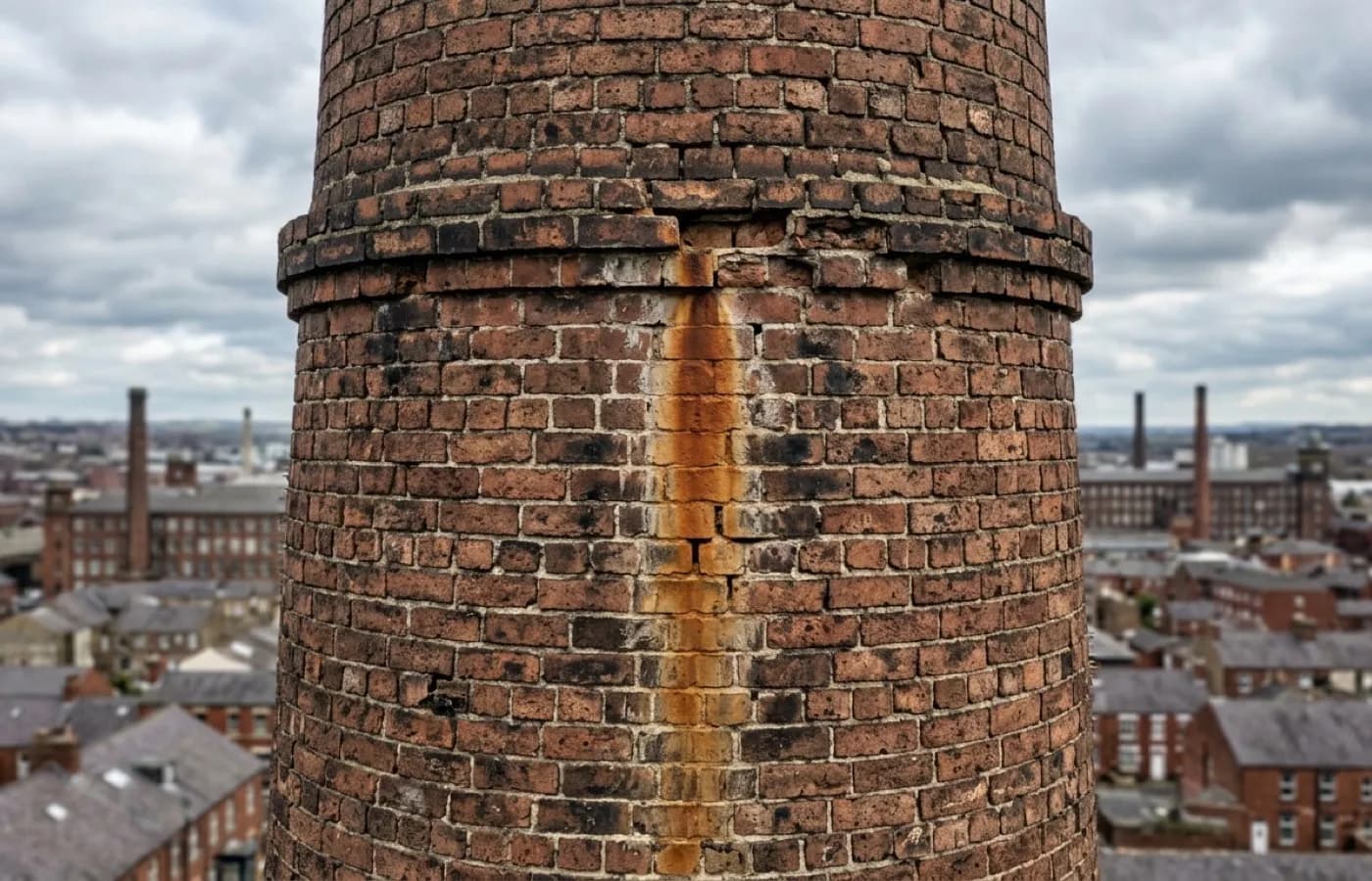Brickwork on a tall Victorian chimney stack with perished pointing and a rust-coloured damp stain running down from a failed joint above